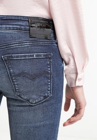 Vaqueros de mezclilla en un tono azul oscuro que presentan un diseño distintivo en el bolsillo trasero con un patrón en zigzag. Parche de cuero negro de la marca en la cintura.