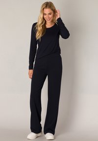 Marineblauw langemouwen top gecombineerd met een broek met wijde pijpen, beide in een zachte stof. Sneakers maken de casual look compleet. Eenvoudig ontwerp met minimale accenten.