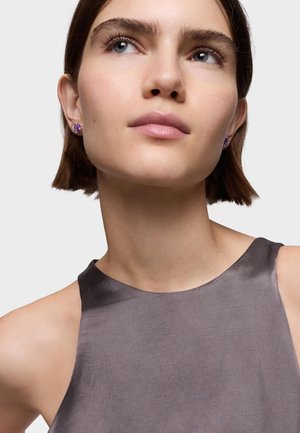 Orecchini a forma di punto viola adornano le orecchie di un modello. Indossa un top senza maniche di satin grigio scuro con una texture liscia e scollatura rotonda.