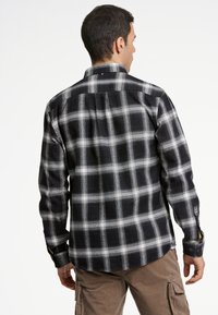 Camicia in flanella a quadri bianco e nero con maniche lunghe, polsini con bottone e giromanica. Tessuto morbido e dettaglio dell'orlo curvo.