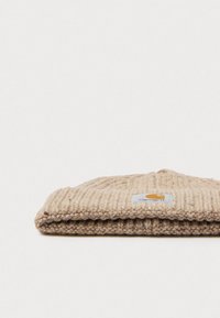 Gorro de punto acanalado beige doblado con un parche del logo de Carhartt sobre un fondo blanco.