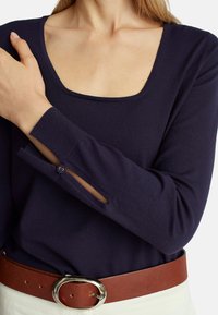 Námořnický pletený svetr se čtvercovým výstřihem, který má knoflíkový rozparek na rukávech. Kombinováno s hnědým páskem a bílou tkaninou.