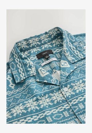 Blaue und weiße gemusterte Bluse mit lockerer Passform, aus strukturiertem Stoff. Mit einem Kragen und Knopfdetails. Markenlabel sichtbar.