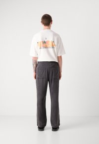T-shirt en coton blanc avec un motif de fruits et le texte "ORANGE COUNTY" ; associé à un pantalon noir gris décontracté avec une taille élastique.