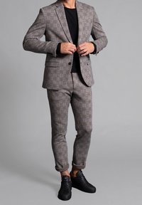 Szary w kratę garnitur z czarnymi akcentami. Dopasowana marynarka i slim-fit spodnie z podwiniętymi mankietami, zestawione z czarnymi sneakersami. Gładka tekstura.