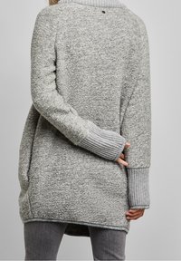 Grå löst stickad tröja med ribbade mudd och nederkant, med rund halsringning och en hög-låg design. Texturerat tyg med en mjuk yta.