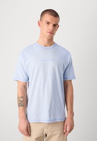 Světle modré tričko s krátkým rukávem, na kterém je uprostřed vyšitý text "SCOTCH & SODA". Měkká bavlněná tkanina, uvolněný střih a kulatý výstřih.