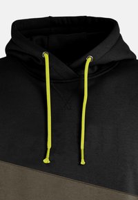 Sudadera negra con un acento inferior verde oliva, que presenta una gran capucha y cordones amarillos brillantes. El material parece suave con una textura lisa.