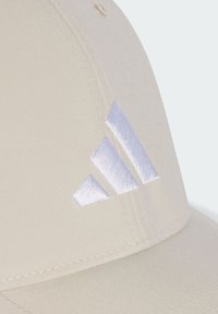 Béžová baseballová čepice s hladkým textilním povrchem, na přední straně s vyšitým bílým logem se třemi pruhy. Zakřivený kšilt.