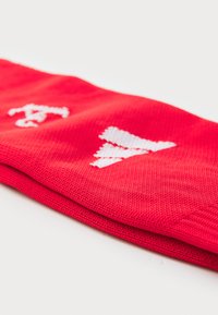Bandeau de sport rouge en tissu texturé, arborant des logos blancs brodés sur le devant. Le design est simple et fonctionnel.