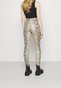 Tight, glänsande byxor med ormskinnsmönster i beige och grå nyanser, med en slät textur och ankellång design, matchade med svarta plattformstövlar.