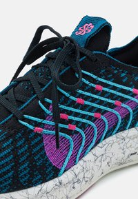 Černá sportovní obuv s texturovaným svrškem s modrými a růžovými akcenty, zaoblenou špičkou a lehkou podrážkou se skvrnitým vzorem. Šněrovadla jsou výrazně vidět.