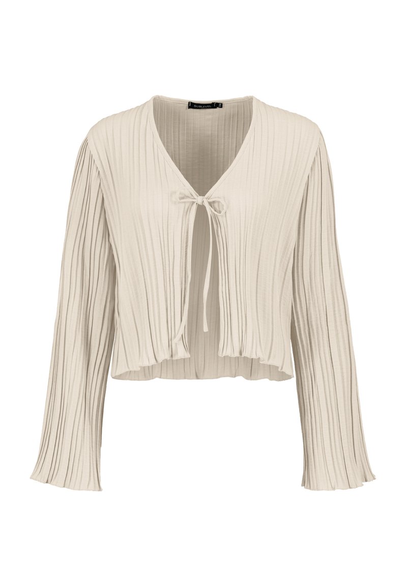 Light beige cropped blouse with long sleeves, featuring vertical pleats and a tie closure at the neckline. Soft, textured fabric.