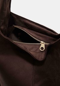 Borsa tote in suede marrone con tasca con zip. L'interno presenta una fodera in tessuto liscio e una cerniera dorata con un tirazip.
