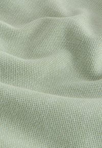 Gros plan sur un tissu vert clair texturé avec un motif tissé et des plis doux créant des ombres légères.