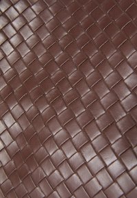 Cuero trenzado marrón con una superficie texturizada que presenta patrones cuadrados y resaltes, mostrando una artesanía intrincada.