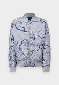 Quilted bomber jacket in light gray with blue floral swirl pattern. Features a front zipper, ribbed cuffs, and two side pockets.