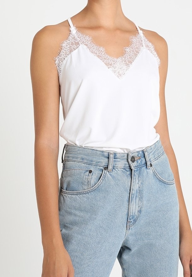 Camisola bianca con pizzo sui bordi delle spalle e del collo, abbinata a jeans in denim azzurro a vita alta. Tessuto morbido.