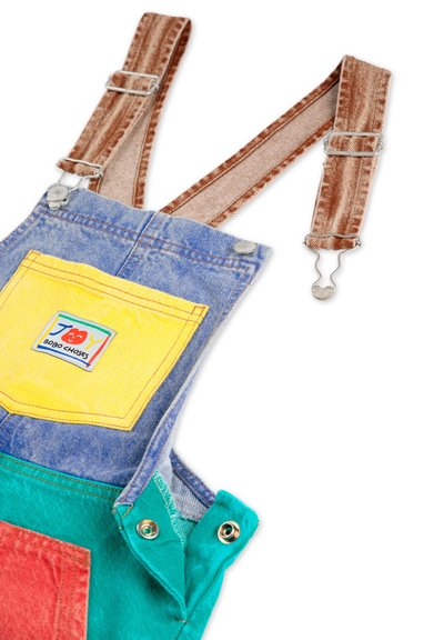 Denim overalls with adjustable brown straps, featuring a yellow pocket and green and red accents. Notable hardware includes metal snaps.