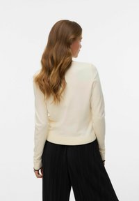 Crèmekleurige trui met lange mouwen en een ronde halslijn, zachte gebreide textuur en geribbelde zoom, gecombineerd met geplooide zwarte broek.