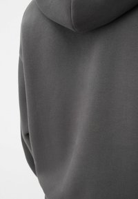 Felpa con cappuccio in cotone grigio, caratterizzata da una texture morbida, vestibilità comoda, cappuccio con cordino e dettagli di cucitura evidenti sulla schiena e sulle spalle.