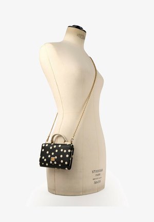 Bolso negro con lunares blancos y una correa de cadena dorada expuesto en un maniquí beige para prendas.