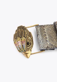 Fibbia a forma di uccello in metallo dorato con strass colorati e piume testurizzate, attaccata a una cintura grigia metallica.