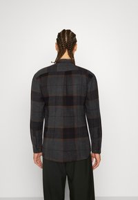 Graues kariertes Flanellhemd mit dunklen und hellen Akzenten, langen Ärmeln, geknöpften Manschetten und einem geraden Kragen, Rückansicht.