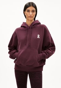 Bordeaux oversized hoodie met een voorkeeltas en geborduurd lintlogo. Gepaard met zwarte en bordeaux gestreepte leggings. Zachte textuur.