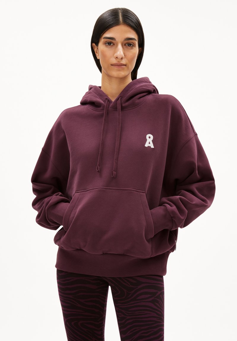 Bordeaux oversized hoodie met een voorkeeltas en geborduurd lintlogo. Gepaard met zwarte en bordeaux gestreepte leggings. Zachte textuur.