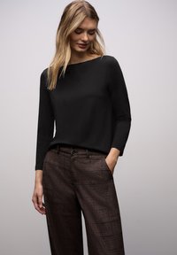 Czarna bluzka z długim rękawem i kwadratowym dekoltem, zestawiona z brązowymi spodniami o szerokich nogawkach z wzorem, zapinanymi na guziki i posiadającymi boczne kieszenie.