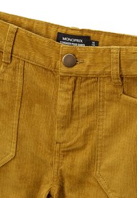 Pantalons en velours côtelé jaune doré avec une texture ribbed verticale, dotés d'un bouton en métal et d'une étiquette portant la mention Monoprix.