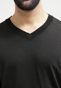 Czarna koszulka z dekoltem w serek, z teksturowanego materiału i prążkowanym dekoltem, zaprojektowana z myślą o dopasowanym wyglądzie. Gładka powierzchnia bez wzorów.