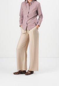 Koszula zapinana na guziki w czerwono-białe paski, beżowe spodnie o szerokich nogawkach oraz baleriny w cętki lamparta, prezentujące luźne dopasowanie i miękkie tekstury.