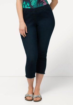 Jean capri bleu marine avec une taille élastique et un ourlet effiloché. Le matériau semble être du jean avec une texture lisse. Style décontracté avec un minimum de détails.