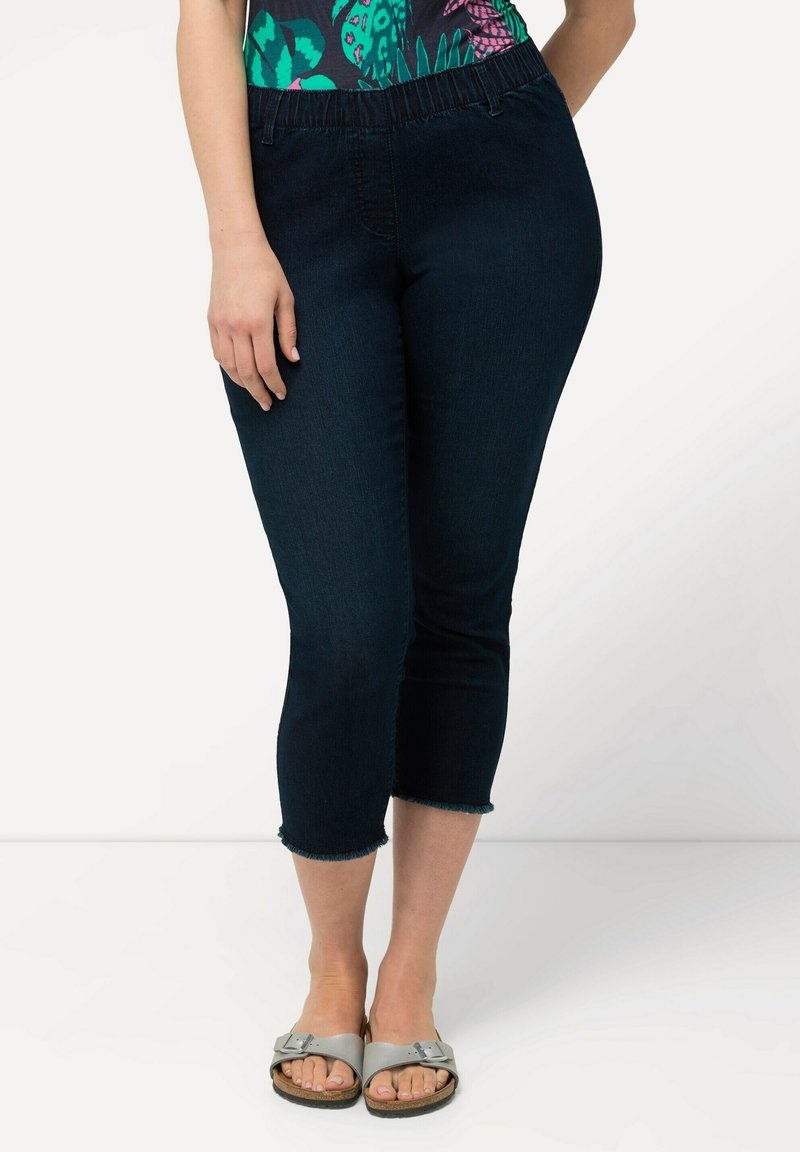 Jeans capri blu scuro con cintura elastica e orlo sfrangiato. Il materiale sembra denim con una texture liscia. Stile casual con dettagli minimi.