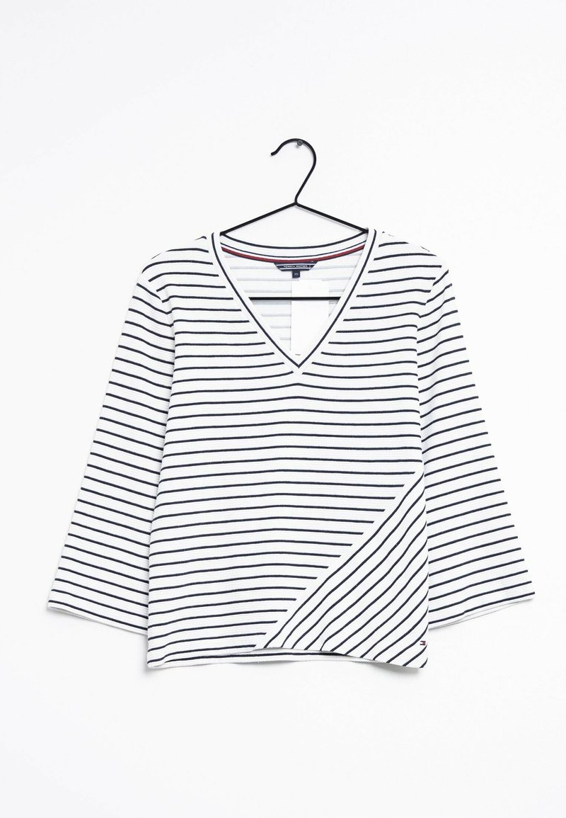 Vit V-ringad topp med horisontella marinblå ränder, trekvartsärmar och en asymmetrisk nederkant med en liten logotypdetalj.