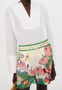 Haut à manches longues blanc à rayures avec un col en V et un short coloré à motifs avec un cordon de serrage. Accents notables en vert, rose et bleu.