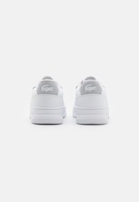 White leather sneakers featuring a flat sole, rounded toe, and grey logo accents on the heel. Minimalist design with textured details.