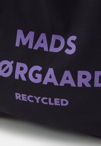Sac en tissu noir avec un texte violet audacieux indiquant "MADS ØRGAARD RECYCLED." Texture lisse, forme rectangulaire, design minimaliste.