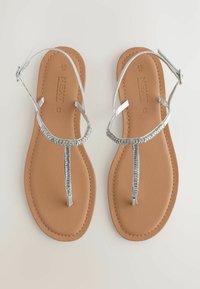 Sandali piatti argento con un design a trama per le cinghie, posizionati su una soletta sintetica color cammello e una suola liscia.