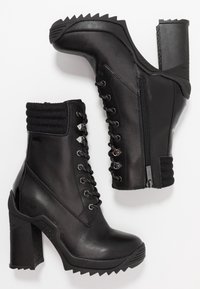 Botas negras hasta el tobillo con un puño de punto texturizado, parte delantera con cordones, cierre de cremallera y tacones dentados. Fabricadas en cuero suave con acentos metálicos.