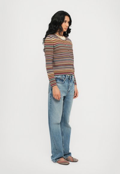 Cardigan a righe a maniche lunghe con scollatura tonda, abbinato a jeans azzurri a vestibilità rilassata e ballerine a righe multicolori.