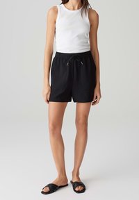 Černé texturované šortky s elastickým pasem a šňůrkou. Spárováno s bílým žebrovaným tílkem a černými skluznicemi.