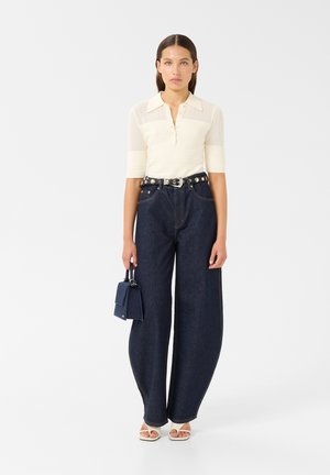 Cream ribbed polo shirt with short sleeves, high-waisted dark blue wide-leg jeans, silver-accented belt, and small blue handbag.