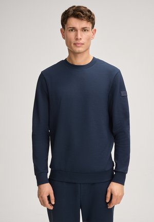 Marineblauwe sweatshirt van een zachte stof, met een ronde hals, lange mouwen en een zijpatch met logo, gecombineerd met bijpassende broek.