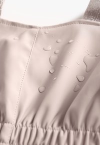 Lys pink vandtæt stof med synlige vanddråber. Har samlet elastik forneden og blændende stropper. Glat tekstur.