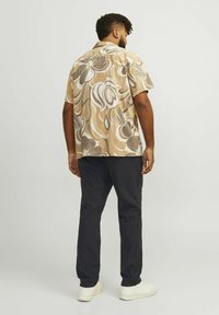 Camisa de manga corta en beige con un patrón floral en espiral, combinada con pantalones oscuros de color navy y zapatillas blancas, vista desde atrás.