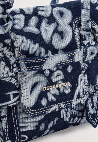 Gros plan d'un sac à main en denim bleu avec un imprimé en style graffiti blanc et un petit logo métallique DSQUARED2 sur le rabat de la poche avant.