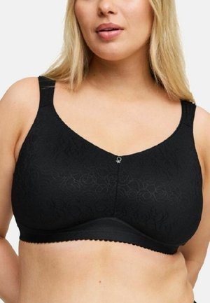 Blond vrouw draagt een zwarte draadloze beha met een subtiel bloemenpatroon en een klein decoratief hangertje middenvoor.